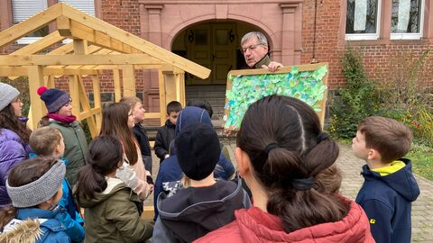 Schülerinnen und Schüler freuen sich gemeinsam mit ihrer Klassenlehrerin Adelheid Ammon über ihr Holz-Spielhaus, das vom Vorsitzenden der Regionalen PEFC-Arbeitsgruppe Hessen e. V., Detlef Stys übergeben wurde.