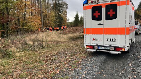 Übung Rettungskette-Forst Rettungswagen von hinten auf einem Waldweg. Im Hintergrund erkennt man Menschen am Wald stehend.