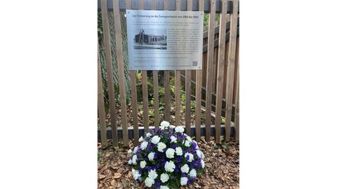Gedenktafel am Standort der Landesbetriebsleitung Kassel. Gedenktafel an Zaun befestigt. Davor liegt ein Blumenkranz.