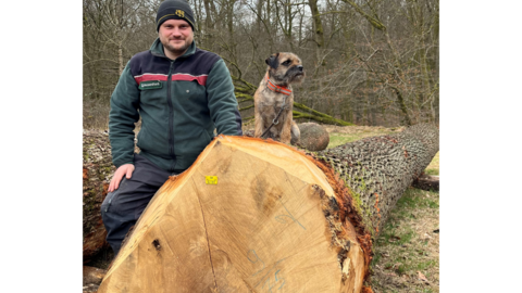 Alexander Zentz, Revierleiter im Revier Linsengericht, neben dem teuersten Eichenstamm der Submission Ein Revierleiter steht mit seinem Hund neben einem Eichenstamm