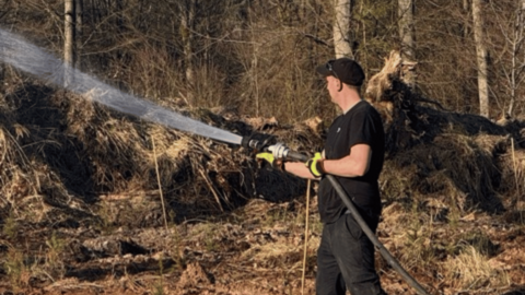 Auf dem Foto sehen sie einen Feuerwehrmann der die Bäume mit einem Wasserschlauch bewässert