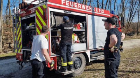 Auf dem Foto sehen sie mehrere Personen die vor einem Feuerwehrauto stehen