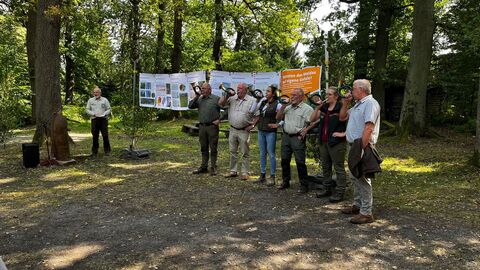 Links Forstamtsleiter Holger-Pflüger-Grone. Vorab der Auftritt einer Bläsergruppe mit dem Signal „Begrüßung“. Jagdhornbläser vor Waldkulisse