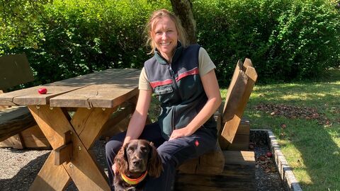 Neue Funktionsangestellte Technik im Forstamt Rotenburg: Katrin von Bodelschwingh Eine Försterin sitzt mit ihrem Jagdhund auf einer Holzbank unter einem Apfelbaum und lächelt den Betrachter an.
