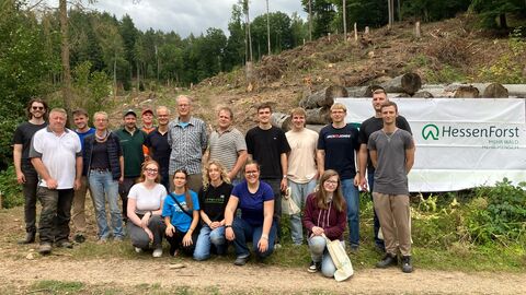 Die Gruppe der Helferinnen und Helfer der PFlanzaktion steht vor der Fläche und einem HessenForst-Banner