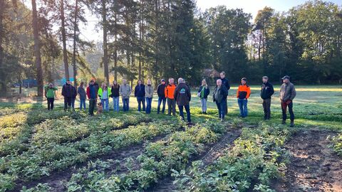 Eine Gruppe steht an einem Verschulbeet und hört aufmerksam dem Mitarbeiter der Baumschule zu. 