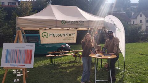 HessenForst zeigt Flagge bei den Taunus Klimatagen 2025 Zwei Menschen stehen vor einem Pavillon und Exponaten des Landesbetriebes HessenForst