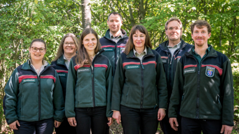 Eine Gruppe Försterinnen und Förster steht vor einem Waldhintergrund. 