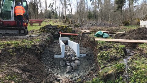Baustelle der Wasserführung mit Bagger und Baumaterialien an einer Quelle.