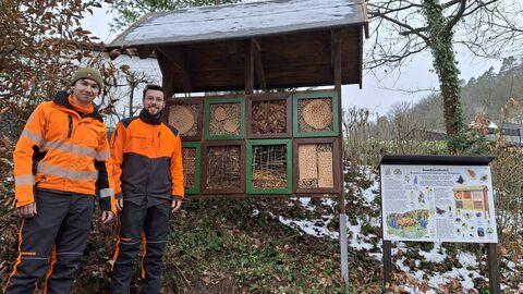 Zwei junge Männer in Signalforstkleidung stehen vor dem erneuerten Insektenhotel. 