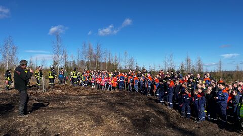 Der Revierleiter Hartwig Holzberg steht vor einer großen Gruppe von Kindern und Jugendlichen in Feuerwehrkleidung und bedankt sich für das geleistete Engagement. 