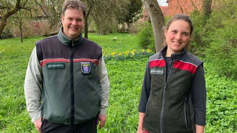 Zwei Menschen in Forstkleidung stehen in einem Garten und lächeln den Betrachter des Bildes an.