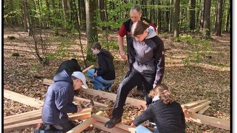 Zwei Kinder bauen eine Hochsitzleiter unter Aufsicht des Forstamtsleiters. 