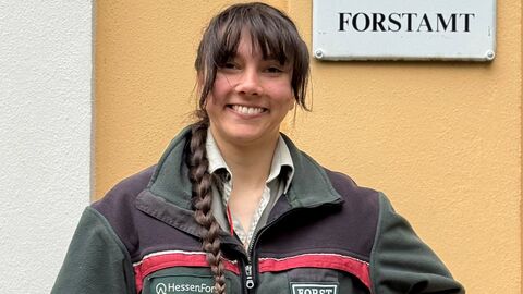 Eine Frau in Forstdienstkleidung vor dem Forstamt. 