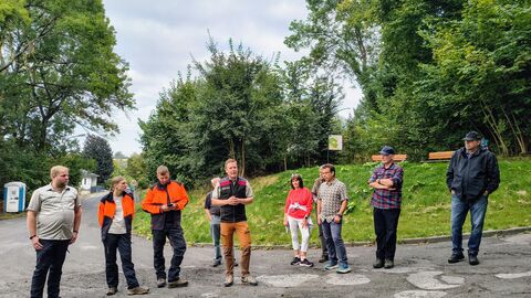 Waldbegang: Eine Gruppe Förster steht auf einer Straße vor dem Waldrand mit weiteren Bürgern. Der Forstamtsleiter referiert. 