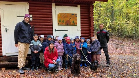 Förster, Kinder und Erzieher vor der Saunahütte in Blockhausbauweise. 